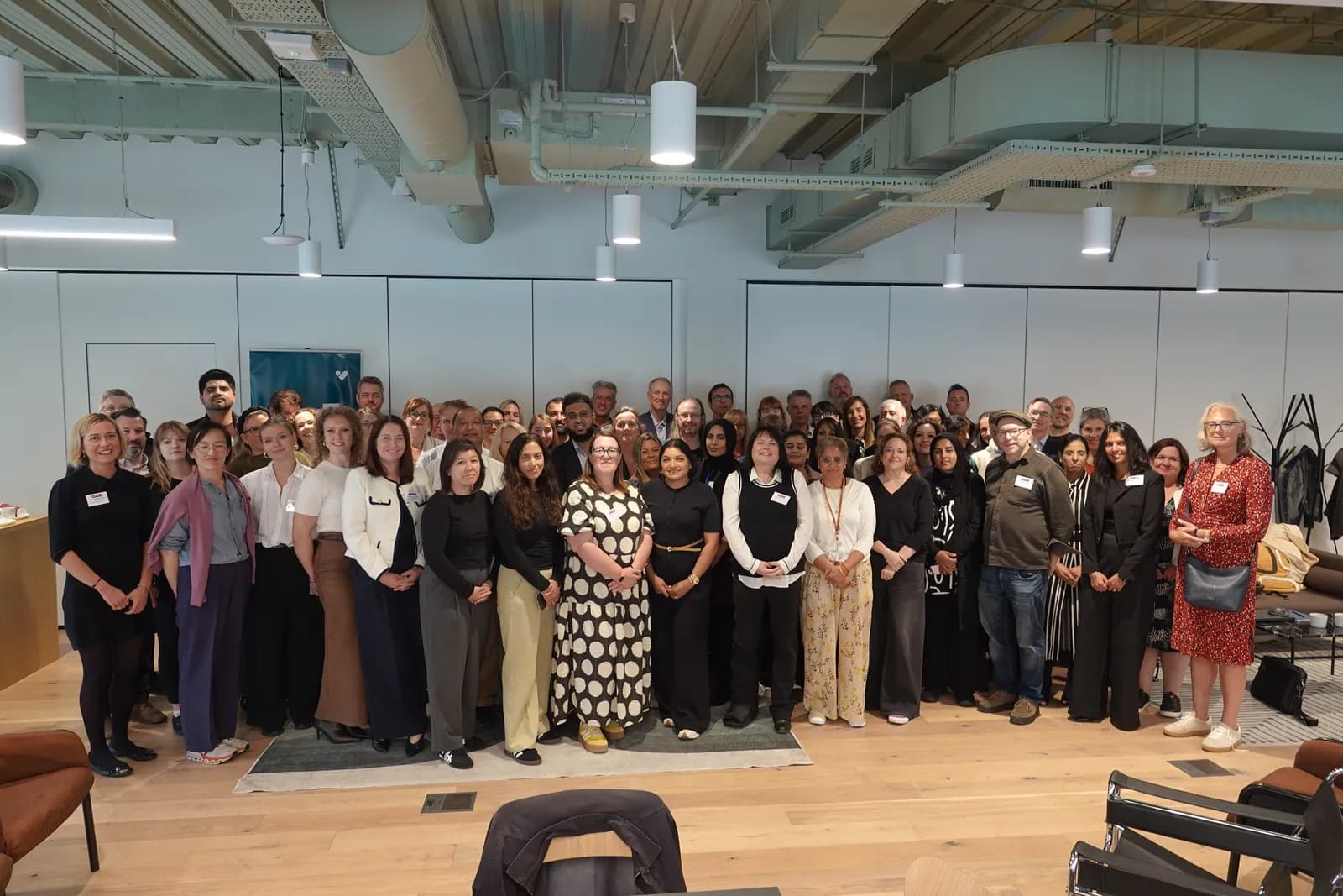 A large group of diverse professionals, men and women, pose for a group photo in a modern office space.